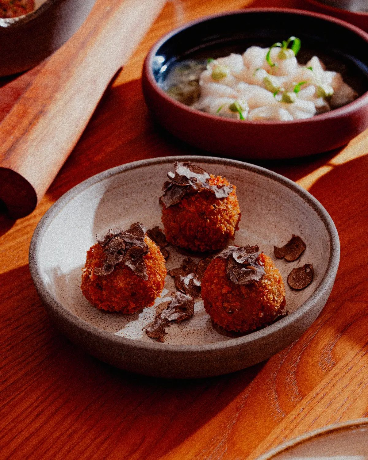 Tres croquetas cubiertas de láminas de trufa en un plato de cerámica