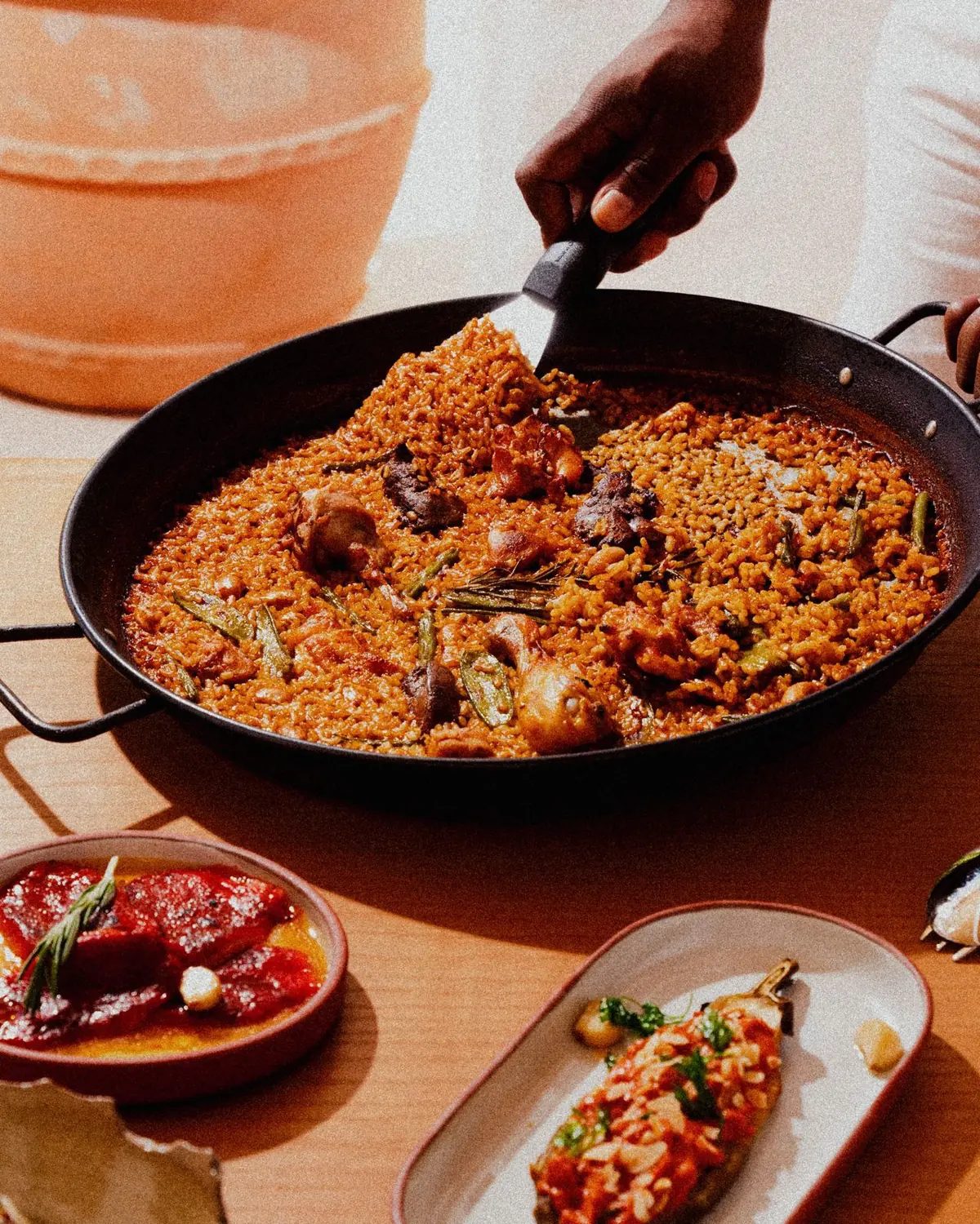 Paella en paellera con verduras y carne, junto a pimientos asados y berenjena